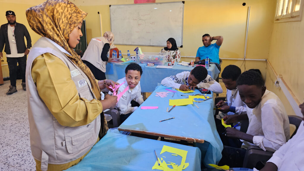 12 November 2023, (GHAT) Libya. Zamzam guides adolescents in Ghat, using scissors to shape petals that represent their growing capabilities and skills they need. Photo: Abdullah Hussein/ UNICEF Libya.